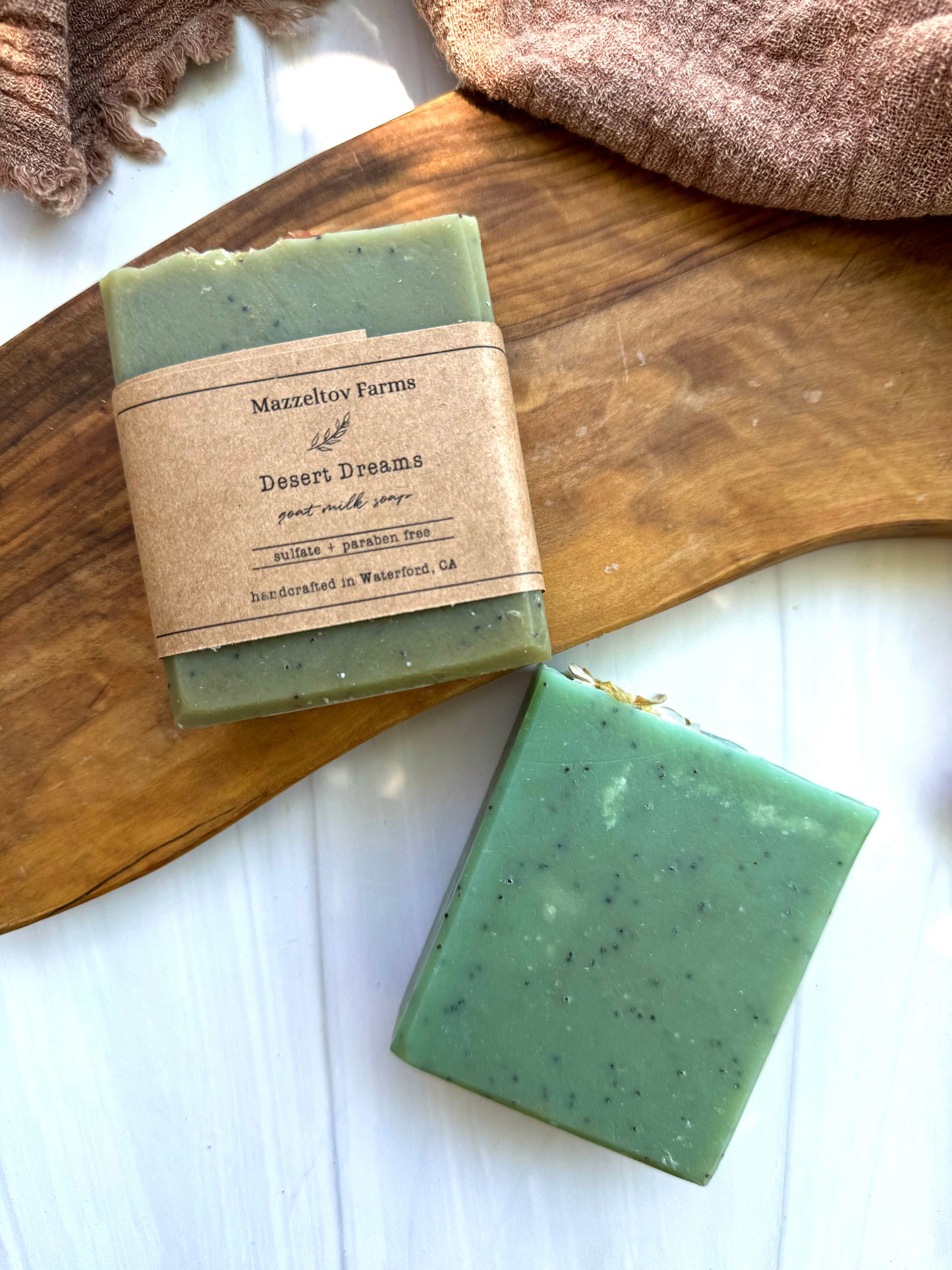 A bar of green goat milk soap with exfoliants, labeled 'Desert Dreams', resting on a wooden surface.