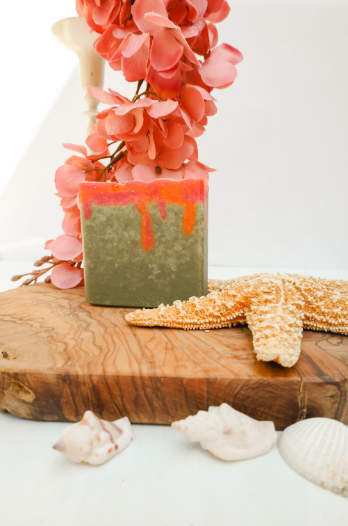 Handmade soap with a red center on a wooden board with flowers and seashells.